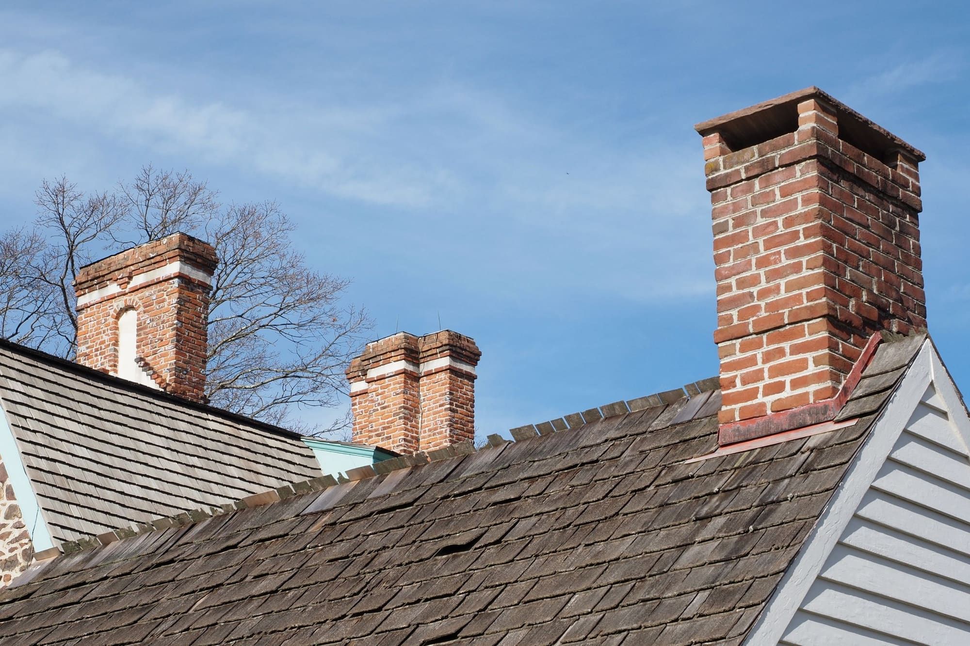 Three older red brick chimneys with corbelled tops rising from wood shingle roofs on an old clapboard house