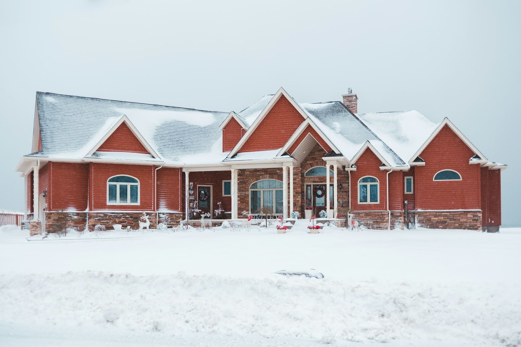 Red house with several gables, arched windows and a small chimney, its roof and yard covered in snow under a gray sky