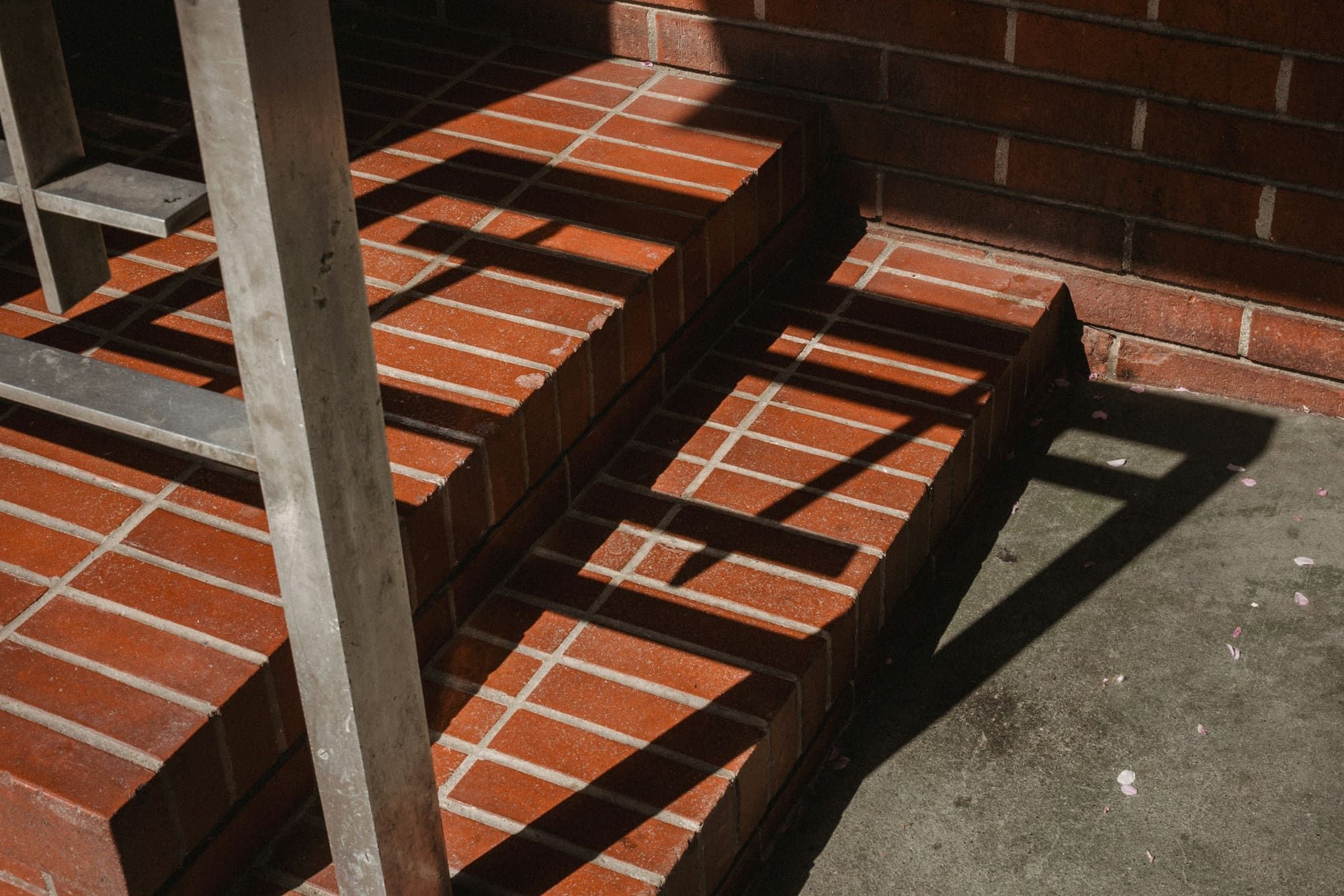 Red brick steps with light mortar joints at a brick wall, crossed by the shadow of a ladder