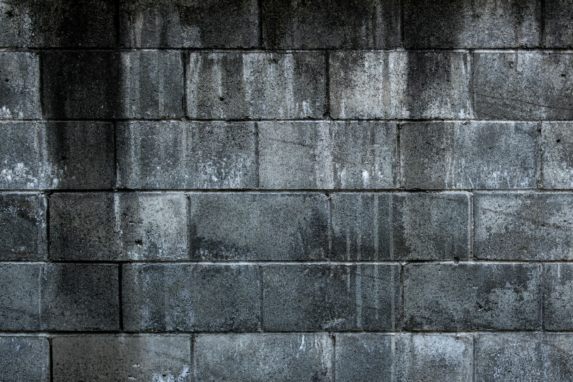 Concrete block wall in running bond with dark water staining running down from the top courses