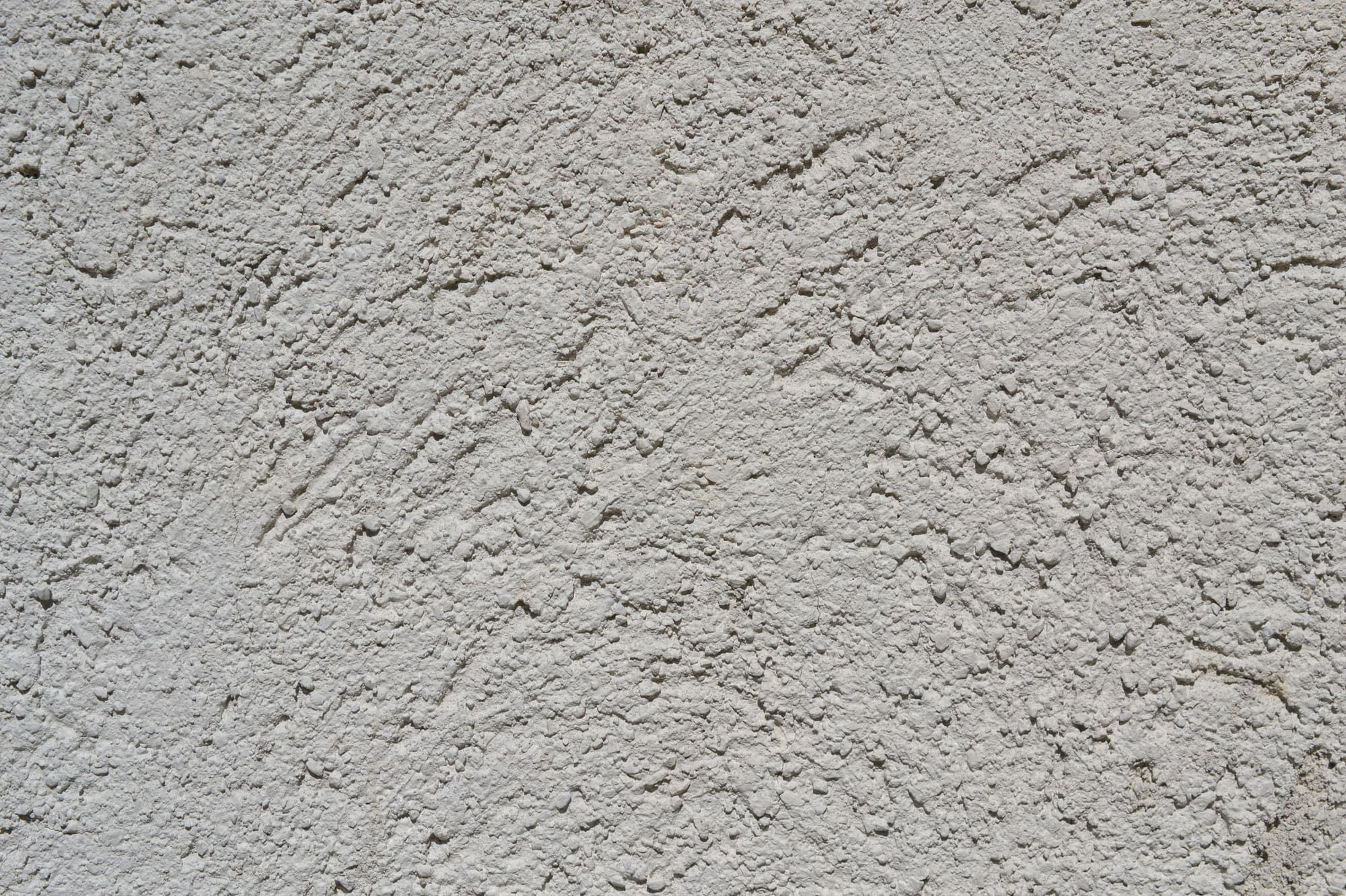 Close-up of a light gray stucco finish with a coarse, pebbly dash texture and shallow trowel sweeps