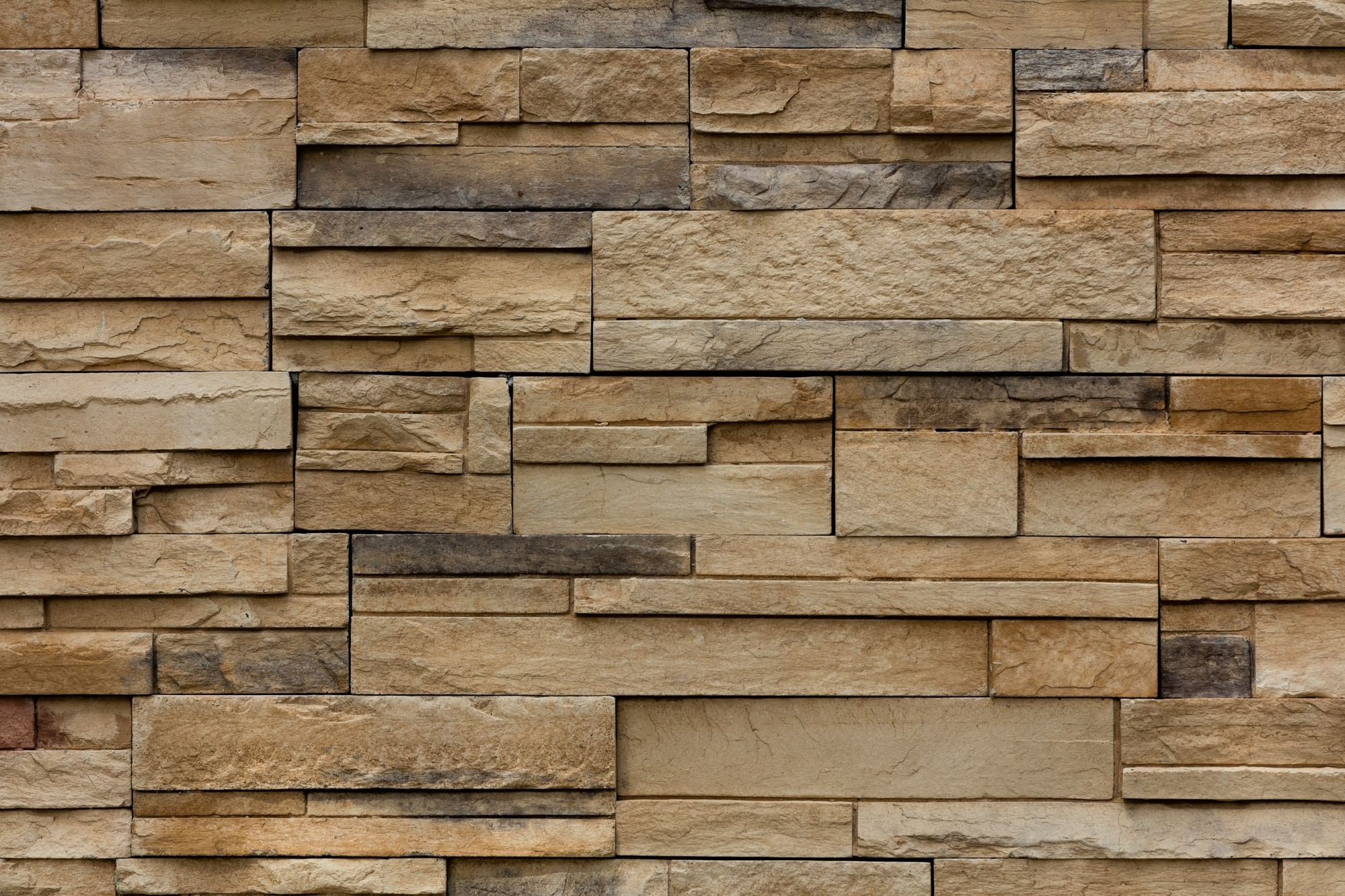 Close-up of tan and brown ledgestone veneer, thin stacked courses fitted tight with no visible mortar joints