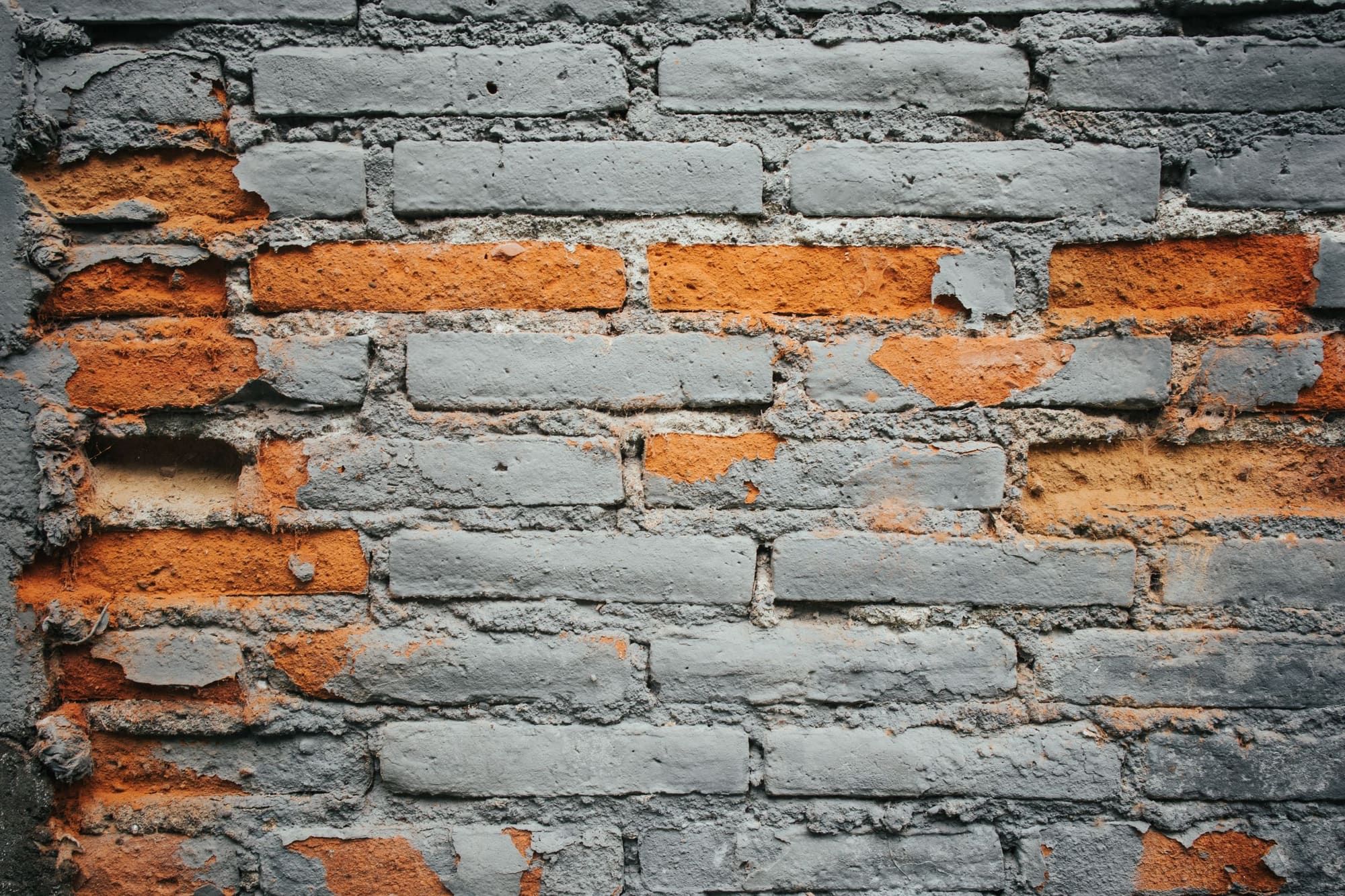 Close-up of a painted brick wall where the faces of several bricks have spalled off, exposing the soft orange clay underneath